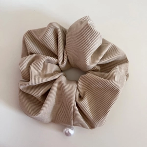 Detailed texture of light brown corduroy scrunchie with a white pearl pendant decoration