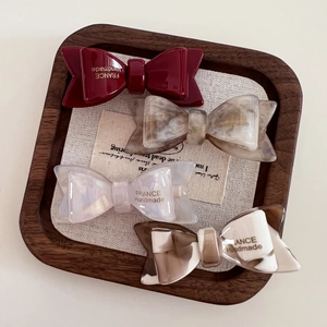 Close-up of four acetate bow hair clips in marble and pearl colors on a wooden tray