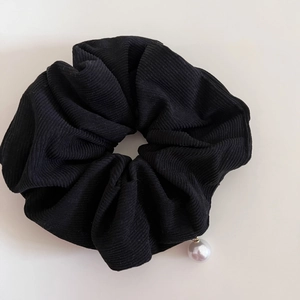 Macro shot of black corduroy scrunchie texture with white pearl pendant detail