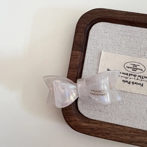 Detail of pearlescent white bow hair clip with France Handmade text on wooden tray