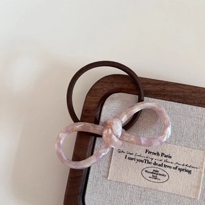 Close-up of pink marbled acetate bow hair tie on a wooden display tray for a French look