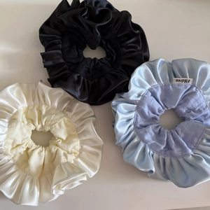 Close-up of ruffled satin scrunchies in black, cream and light blue with fine fabric texture