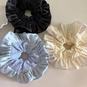 Detailed macro view of three oversized satin hair scrunchies in black, light blue, and beige