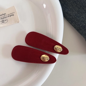 Zwei rote Samt-Haarspangen in Tropfenform mit goldenen Metallplättchen auf Keramik