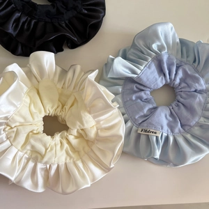 Detailed close-up of glossy satin scrunchies in black, beige, and blue with ruffled texture