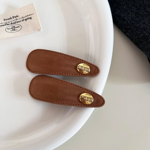 Nahaufnahme brauner Wildleder-BB-Haarspangen mit goldenen Knöpfen und feiner Gravur