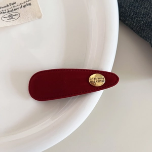 Nahaufnahme einer Haarspange aus rotem Samt mit goldenem Metallknopf und Motivationsgravur