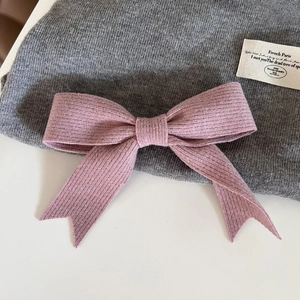 Gros plan d'une pince à cheveux nœud en tricot rose sur fond de tissu gris texturé