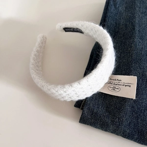 Detailed close-up of a white knitted headband with a black Hand Made fabric label