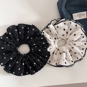 Detail showing two pleated polka dot scrunchies in black and beige on white background