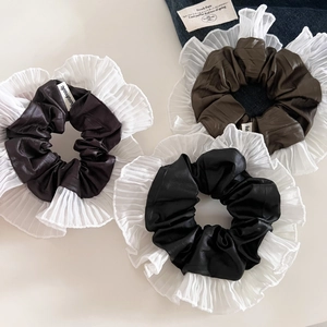 Détail de trois chouchous en cuir avec bords en dentelle blanche plissée et étiquettes