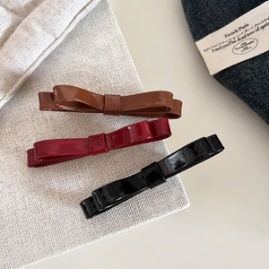Close-up of three glossy leather double-layered bow hair clips in brown, red, and black