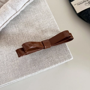 Close-up of a glossy brown double-layered leather bow hair clip on a beige textured bag