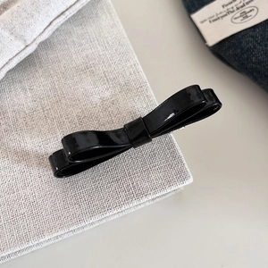 Close-up of black double-layered faux leather bow hair clip on textured fabric surface