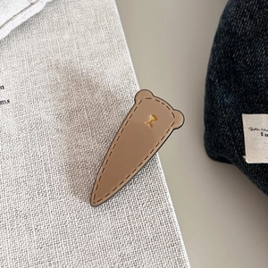 Detail of bear ear acetate hair clip with golden emblem on denim background