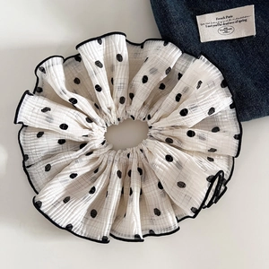 Close-up of a white polka dot scrunchie with layered ruffles and black edge stitching