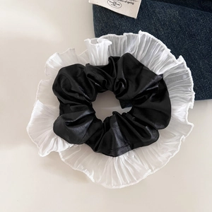 Détail d'un chouchou en similicuir noir avec des bords plissés en organza blanc