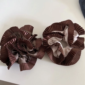 Close-up of two chestnut brown pleated satin scrunchies with elegant double-layered texture