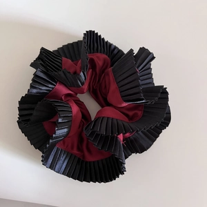 Detailed macro of a pleated satin scrunchie featuring a dual-layer burgundy and black design
