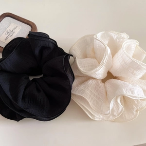 Detail view of large pleated fabric hair scrunchies in black and creamy white colors