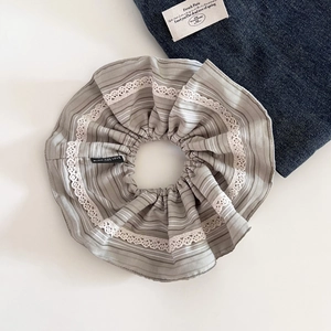 Detailed view of gray striped fabric scrunchie with lace edge and black logo label