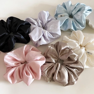 Detail of assorted glossy satin scrunchies in pastel colors with minimal woven labels