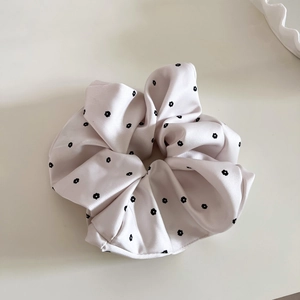Detailed shot of light pink satin floral scrunchie with soft silk texture on beige surface