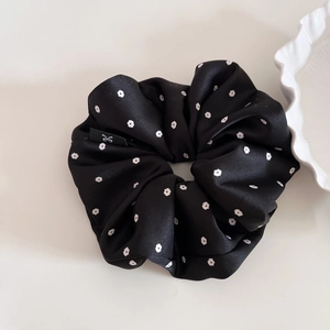 Detailed macro view of black satin floral scrunchie with a logo label and white flowers