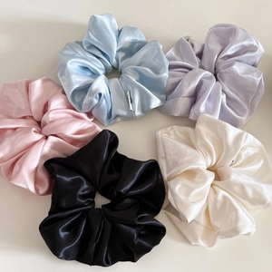 Detail view of five assorted satin silk scrunchies in pastel colors with glossy texture