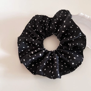 Gros chouchou en satin noir à pois blancs présenté sur un fond esthétique blanc épuré