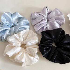 Macro detail of four glossy satin hair scrunchies in blue, purple, white, and black