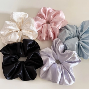 Close-up of five large satin scrunchies in assorted colors with a glossy silk texture