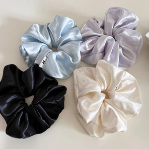 Detail of four colorful silk satin hair scrunchies showing smooth glossy texture and labels