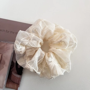 Détail du chouchou en dentelle beige avec broderie florale et texture en résille