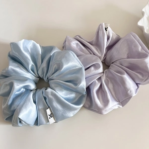 Detail of blue and purple satin hair scrunchies with glossy texture and small logo labels
