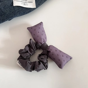 Détail d'un chouchou gris à volants avec un nœud lilas à pois sur fond blanc épuré