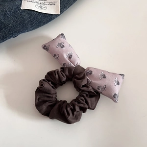 Détail d'un chouchou vintage avec nœud à motif abeille violet sur tissu marron foncé