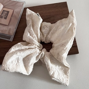 Detailed close-up of beige floral lace scrunchie with long ribbons on wooden surface