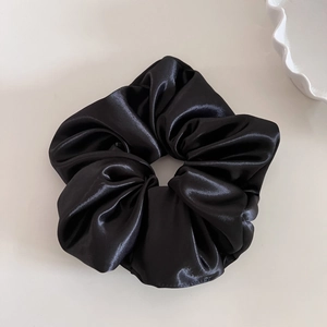 Detail view of a black satin scrunchie with glossy texture on a light beige background