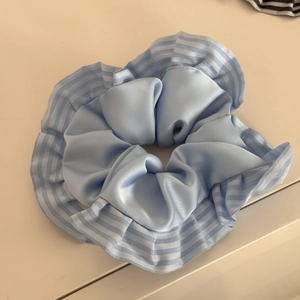 Nahaufnahme von hellblauem Satin-Haargummi mit eleganten Rüschenkanten und Streifenmuster
