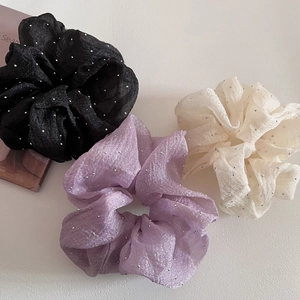 Detail of three oversized organza scrunchies in black, purple, and cream with glitter dots