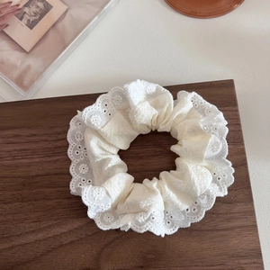 Dettaglio macro dello scrunchie in pizzo di cotone bianco con trame ricamate a strati
