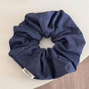 Gros plan du chouchou en denim bleu foncé montrant la texture du tissu et l'étiquette