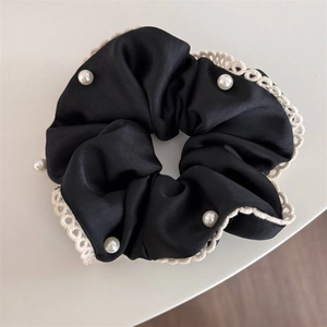 Macro detail of black satin scrunchie with white lace trim and faux pearl accents