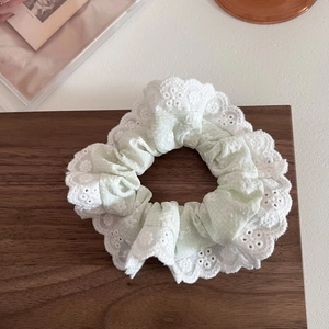 Dettaglio di scrunchie verde chiaro con ricamo in pizzo bianco e motivi traforati