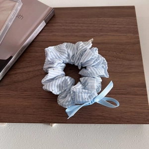 Chouchou rayé bleu clair avec strass et nœud en ruban sur un support en bois
