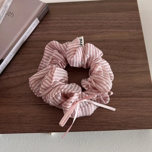Détail d'un chouchou à rayures roses avec strass et un joli nœud sur fond en bois