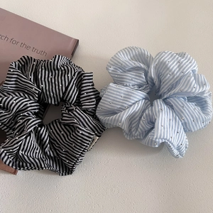 Close-up of two striped hair scrunchies with silver studs on a fabric texture