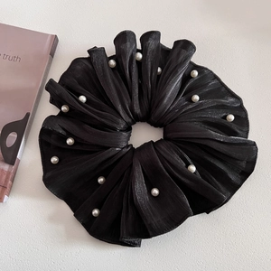 Détail d'un chouchou en organza noir au fini brillant avec d'élégantes perles blanches
