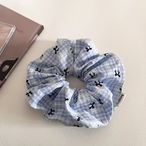 Blue and white checkered hair scrunchie with bow patterns and brand tag on textured surface